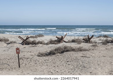 Anti-tank hedgehogs, barbed wire on the beach by the sea (the inscription on the plate translates as - stop - mines) - Shutterstock ID 2264017941