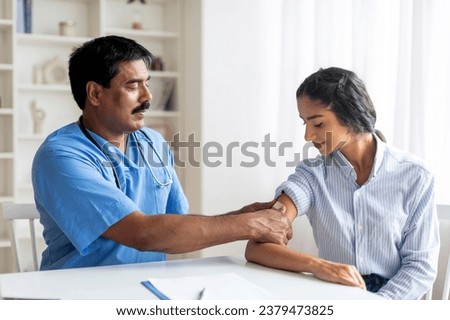 Antiviral Vaccination, Immunization. Middle aged medical worker sticking plaster bandage on patient's shoulder after injection in health centre, young eastern woman getting vaccine in modern clinic