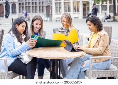 Antwerp, Belgium, 05-21-2021, Lifestyle Portrait Of A Diverse Multiethnic Group Of Four Young Smiling Businesswomen With Smartphones, Notes And Notebook Outside In A Cafe At Work While Having A Drink