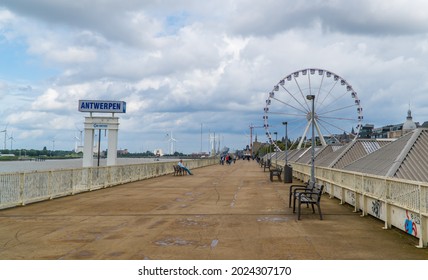 Antwerp, Belgium - August 8, 2021 - people sitting next to Antwerp (Antwerpen) port sign on the Scheldt river with a Ferris wheel