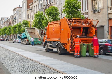 ANTWERP, BELGIUM. July 19, 2017. Municipal Cleaning Service Workers Remove Waste With Orange Garbage Truck. Dumpster Container On Truck