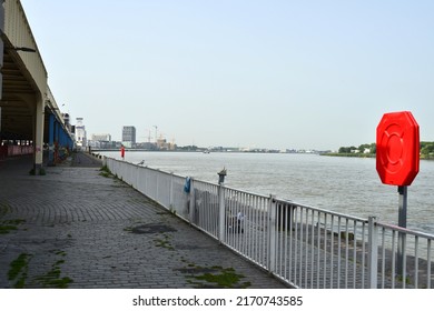 Antwerp city, Province Antwerp, Belgium - June 18, 2022: a view on the Scheldt river quay in diminishing perspective. iN front red cover lifebuoy on a pole. Horizon urban skyline with a tower