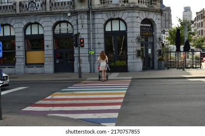 Antwerp City, Province Antwerp, Belgium - June 18, 2022: Pretty Lady With White Dress And Little Child In A Pram Crossing At Red Traffic Lights The LGTBQ  Rainbow Colored Crossroad Corner House Suiker