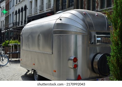 Antwerp city, Province Antwerp, Belgium - June 18, 2022: stationary aluminium design caravan mobile home camper rounded shapes, closed window shutters, stationary abandoned in front of row houses.  
