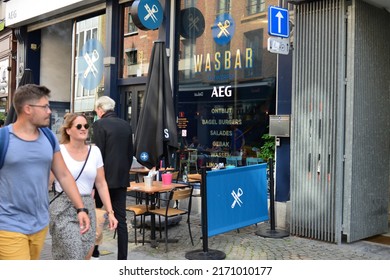 Antwerp city, Province Antwerp, Belgium - June 18, 2022: Caucasian hetero couple walking in front of Wash bar. Outdoors tables café terrace.  Indoors accommodations, wash your clothes during a drink