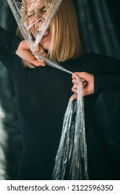 Anxiety Attack. Emotional Crisis. Anger Violence. Art Portrait Of Crazy Disturbed Psycho Woman In Black Screaming Tearing Off Transparent Polyethylene Film Isolated On Dark Background.