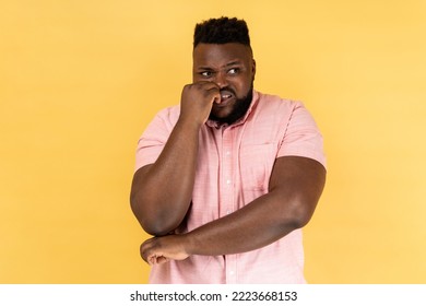 Anxiety disorder. Portrait of stressed out worried man in pink shirt biting nails, nervous about troubles, panicking and looking scared, looking away. Indoor studio shot isolated on yellow background. - Powered by Shutterstock