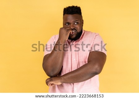 Anxiety disorder. Portrait of stressed out worried man in pink shirt biting nails, nervous about troubles, panicking and looking scared, looking away. Indoor studio shot isolated on yellow background.