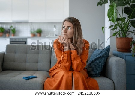 Anxiety woman in stress, looking aside nervously squeezes hands sitting on sofa thinking about problems after receive bad news on cellphone. Worried female feel frustration waiting call on smartphone.