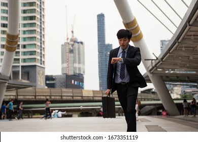 Anxious Asian Chinese Businessman Run And Look At Watch To Check Time On City Walk In Rush Hour. Hurry Young Man Late For Train Transportation, Work, Meeting. Office Life And Business Competition.