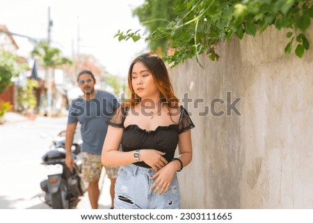 An anxious asian woman notices a creepy man following her for a while. Outdoor scene.