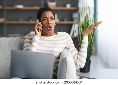 Anxious Black Lady Talking On Mobile Phone And Using Laptop At Home, Emotional African American Woman Having Unpleasant Call Conversation While Working Remotely With Computer At Home, Closeup