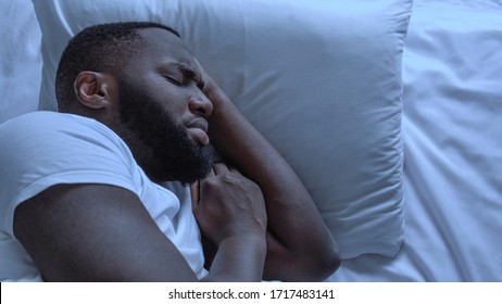 Anxious black man seeing bad dreams during sleeping, suffering from nightmares
