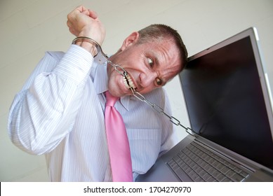 Anxious Businessman Chained To His Laptop Computer Trying To Break Free Of The Handcuffs