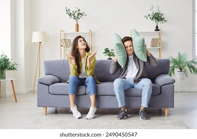 Anxious couple at home, man covering ears with pillow, unhappy irritated family ignoring loud noise sound, feeling stressed of noisy disturbing neighbors, loud music, hating hearing sound of works  - Powered by Shutterstock