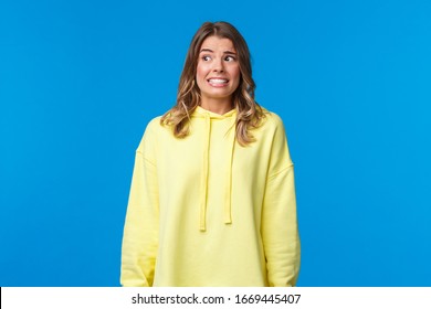 Anxious And Embarrassed, Alarmed Insecure Girl Have Panic And Nervous Thoughts Of Someone Found Out Her Dirty Little Secret, Smile Awkward And Worried Look Around, Stand Blue Background