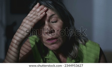 Anxious mature woman struggling with inner thoughts ruminations. Preoccupied expression of a middle-aged female person struggling with mental illness sitting by window at home