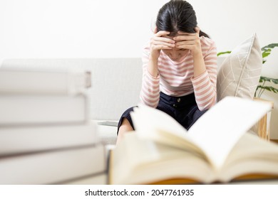 Anxious teenage girl has tension during exam preparation,Stressed worried asian student while studying reading a textbook before final test at her home,afraid of failing the exam,education concept