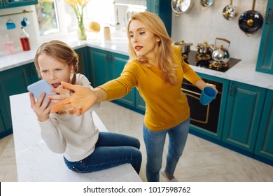 Anxious. Uncontrolled Fair-haired Slim Girl Holding A Phone And Crying While Her Mom Taking It Away