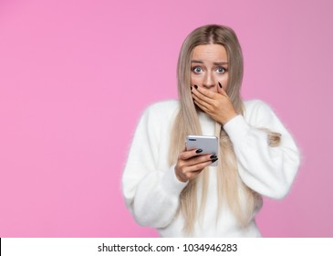 Anxious Young European Blonde Woman Covers Mouth In Shock And Holding Her Phone, Found Out Something Important In Message, Looking At Camera With Wide Opened Eyes/ Human Emotions, Reaction Concept