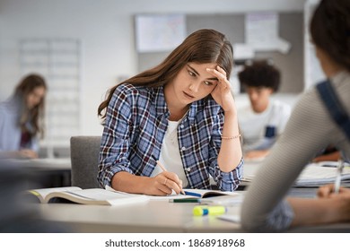 Anxious young woman with hand on head feeling tired while studying at school. College student suffering from headache in classroom. Troubled and stressed girl doing exam that doesn’t know the answers. - Powered by Shutterstock