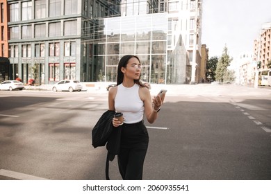 Anxious young woman using map app on her smartphone traveling around city with her mobile phone. Looks to side looking for right street. She is wearing casual black suit.