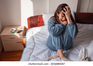 Anxious Young Woman Wearing Pajamas Sitting On Bed In The Morning, Holding Head In Hands, Crying