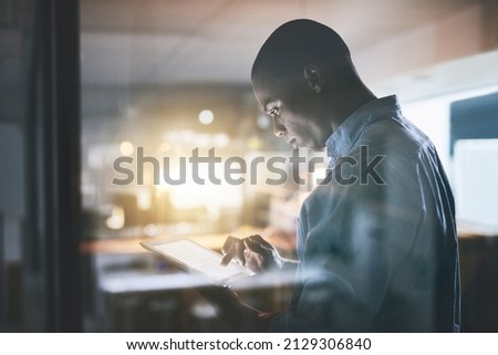 Anything is doable with dedication. Cropped shot of a handsome young businessman using a digital tablet during a late night in a modern office.