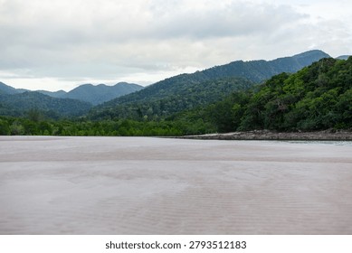 Ao Son Beach features pristine sandy shores and lush green hills. Gentle waves lap against the tranquil coastline. The scenic view includes dense forests and distant mountains under a cloudy sky.