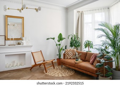 Apartment with bright living room in boho style. Interior design with brown couch, new armchair, decorative fireplace with candles, green house plants in clay pots and rug on the wooden floor - Shutterstock ID 2192332515