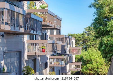 Apartment Building With Attached Garages And Balconies With Potted Plants In San Francisco, CA. Side-view Of Apartment Building Exterior With Gray Wooden Siding And Wooden Balcony Railings.