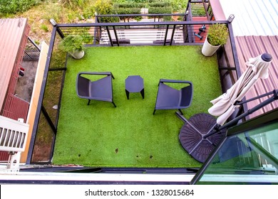 The apartment building's balcony, top view with the black outdoor furniture set and the green artificial grass floor. 