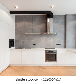 Apartment with contemporary interior. Kitchen in loft style, built in household appliance, electric stove, oven, sink on worktop, wooden laminate on floor and extractor hood on grey wall - Shutterstock ID 1520514617