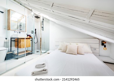 Apartment with exposed wooden beams painted white, glass cabin with bathroom with white porcelain sink on wooden cabinet and mirror with matching frame