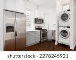 An apartment kitchen with white and grey cabinets, stainless steel appliances, and a stacked washer and dryer. No brands or names.