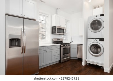 An apartment kitchen with white and grey cabinets, stainless steel appliances, and a stacked washer and dryer. No brands or names.