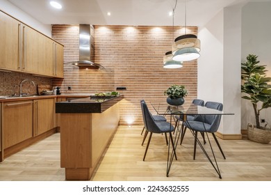 Apartment with open kitchen with wooden furniture with black marble countertop and glass and metal office table with blue velvet upholstered chairs