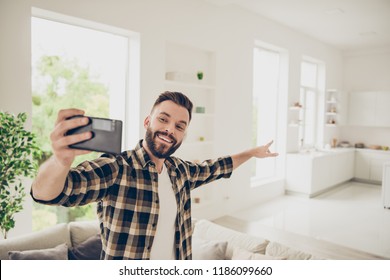 Apartment Purchase Concept. Let's Go And I'll Show You My House! Young Man Make Call On Front Camera Of Modern Smartphone Standing In The Middle Of A Light Room In His Brown Stylish Trendy Shirt