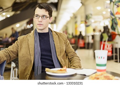 Apathetic Young Man Eating Pizza At The Food Court In A Mall