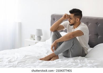 Apathy Concept. Sad Young Arab Guy Sitting On Bed At Home, Portrait Of Depressed Middle Eastern Man Thinking About Problems, Suffering Emotional Breakdown, Feeling Upset And Lonely, Copy Space