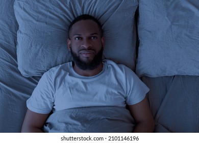 Apathy And Insomnia Concept. Above top view portrait of depressed young black man lying in bed alone and feeeling upset, thinking about problems, feeling lonely, looking up at ceiling - Powered by Shutterstock