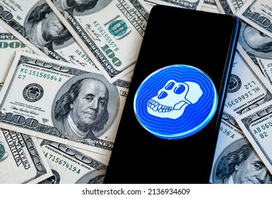 ApeCoin crypto token logo seen on the smartphone which is placed on dollars. New cryptocurrency from NFT Bored Ape Yacht Club. Otherside metaverse. Stafford, United Kingdom, March 18, 2022