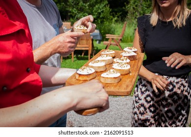 Apero bread with cream and nuts on a wooden platter by a waiter with a red shirt. People are taking a snack on a family party in the garden at home. Communion celebration of a child. 