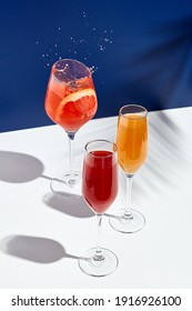 Aperol Drink And Bellini Cocktail On White Table With Blue Background. Sunshine And Palm Leaf Shadow Drink Modern Still Life. Summer, Party, Tropical And Freshness Concept