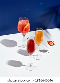 Aperolgetränk und Bellini-Cocktail auf weißem Tisch mit blauem Hintergrund. Sonnenschein und Schatten aus Palmblättern trinken modernes Stillleben. Sommer-, Party-, Tropen- und Frische-Konzept