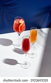 Aperol Drink And Bellini Cocktail On White Table With Blue Background. Sunshine And Palm Leaf Shadow Drink Modern Still Life. Summer, Party, Tropical And Freshness Concept