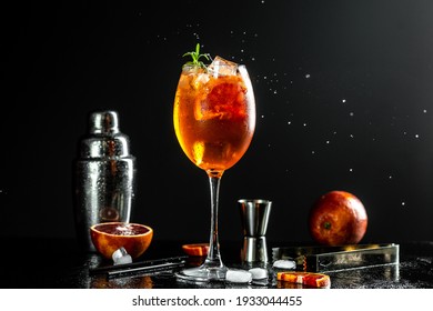 Aperol Spritz Cocktail In Big Wine Glass With Bloody Oranges, Red Bitter, Dry White Wine, Soda, Zest And Ice On Dark Background, Bar Tools.