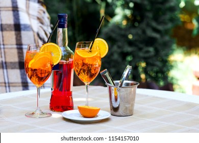 Aperol Spritz Cocktail In Glass And Bottle On The Wooden Table. Two Glasses With A Cocktail And An Ice Bucket.