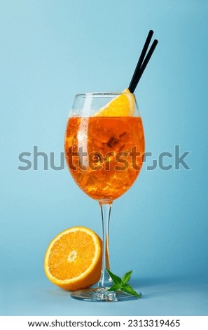 aperol spritz cocktail in glass with straw and slice of orange on blue background