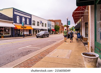 Apex, North Carolina USA-05 14 2022: A Couple Walks Their Dog On The Sidewalk In Downtown Apex